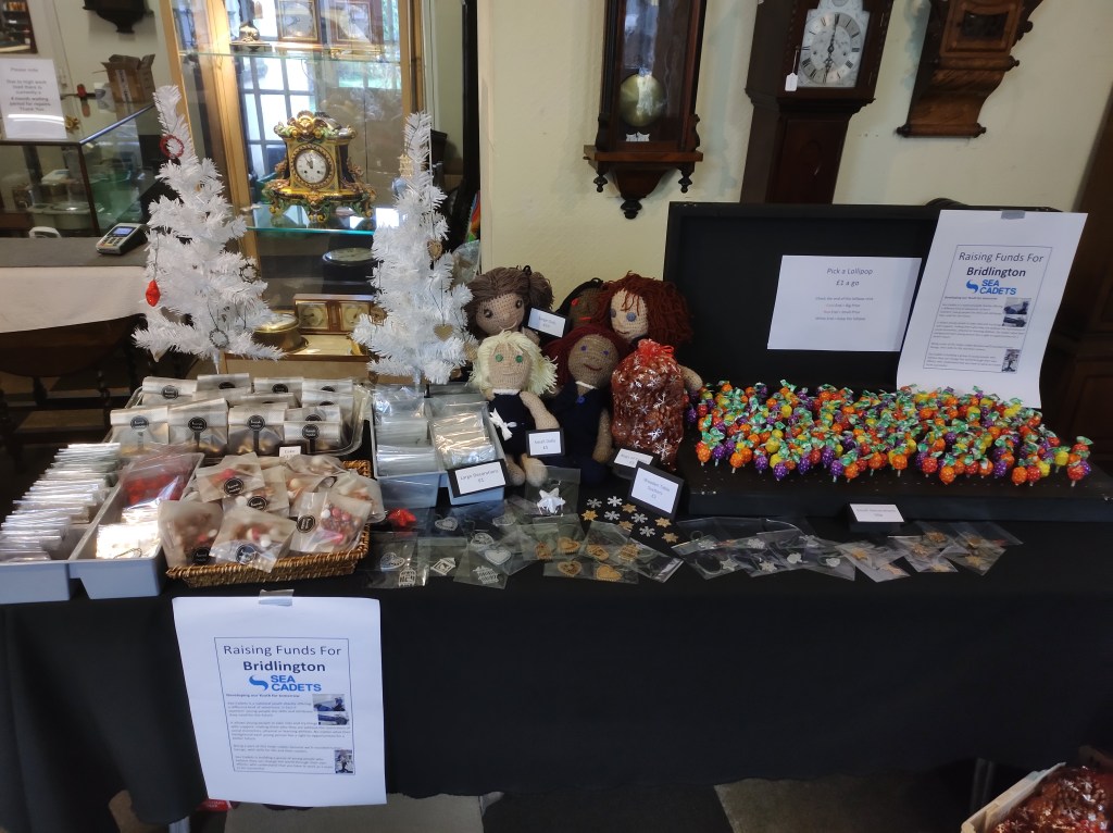 Photograph of table displaying homemade doll, decorations, cakes and lollipops.